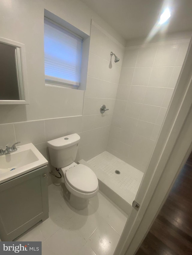 bathroom featuring hardwood / wood-style flooring, toilet, vanity, tile walls, and a tile shower