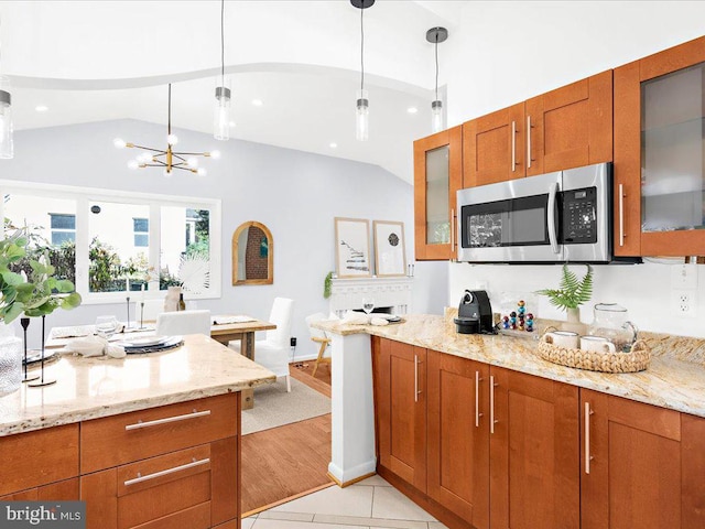 kitchen featuring light stone countertops, light wood-type flooring, a notable chandelier, hanging light fixtures, and lofted ceiling