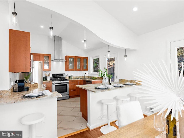 kitchen featuring lofted ceiling, hanging light fixtures, wall chimney exhaust hood, kitchen peninsula, and stainless steel appliances