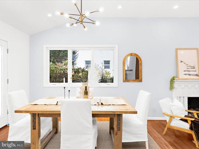 dining room with a brick fireplace, an inviting chandelier, light wood-type flooring, and vaulted ceiling