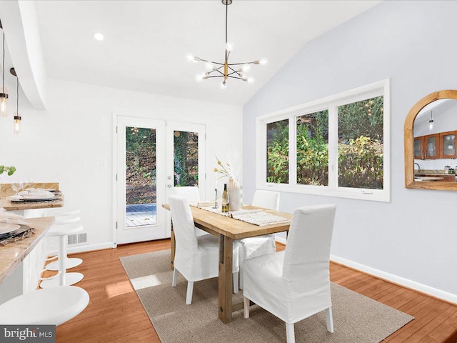 dining space with light hardwood / wood-style floors, an inviting chandelier, and lofted ceiling