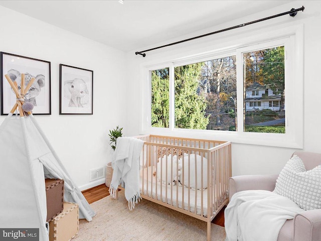 bedroom with multiple windows, hardwood / wood-style floors, and a crib