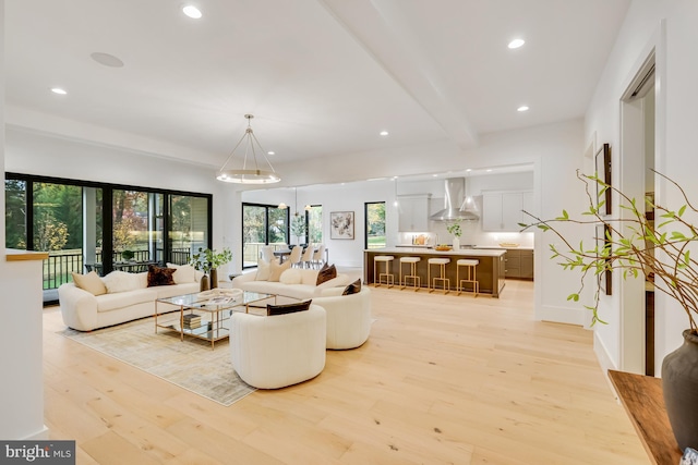 living room featuring an inviting chandelier, beam ceiling, and light hardwood / wood-style floors