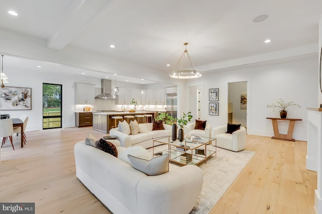 living room with light hardwood / wood-style floors, a notable chandelier, beamed ceiling, and sink