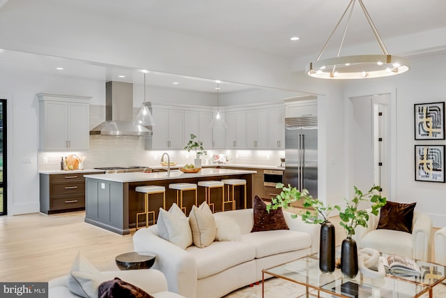 kitchen featuring decorative backsplash, wall chimney range hood, stainless steel appliances, a center island with sink, and pendant lighting