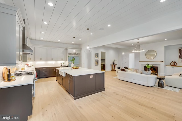 kitchen with white cabinets, an island with sink, light wood-type flooring, range, and decorative light fixtures