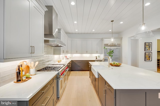 kitchen with wall chimney exhaust hood, decorative light fixtures, premium appliances, and a large island with sink