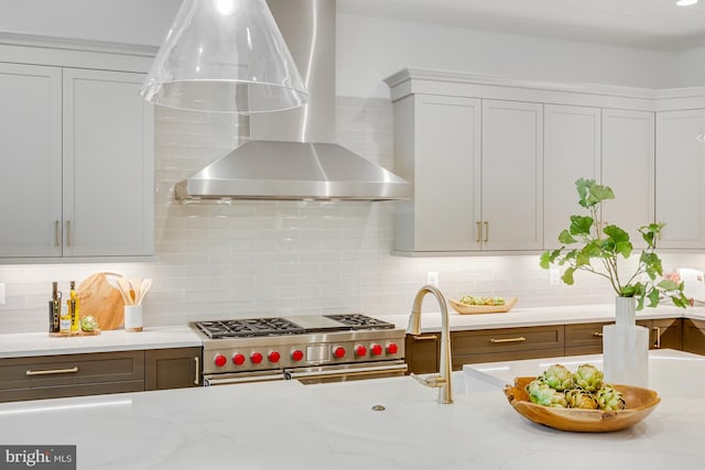 kitchen featuring light stone counters, wall chimney range hood, stainless steel stove, and tasteful backsplash