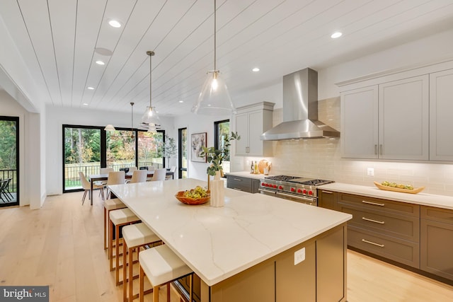 kitchen featuring light hardwood / wood-style floors, wall chimney exhaust hood, a center island, and range with two ovens