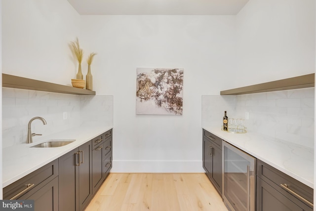 kitchen featuring decorative backsplash, beverage cooler, light wood-type flooring, sink, and light stone counters