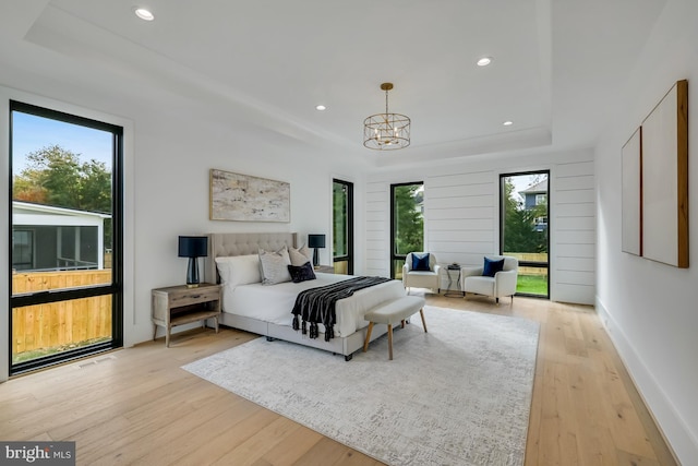 bedroom featuring a chandelier, light hardwood / wood-style flooring, multiple windows, and a raised ceiling