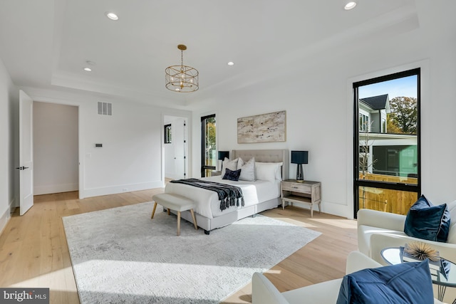 bedroom featuring a notable chandelier, light hardwood / wood-style flooring, and a raised ceiling