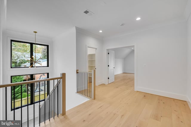 hall with a notable chandelier, ornamental molding, and light wood-type flooring