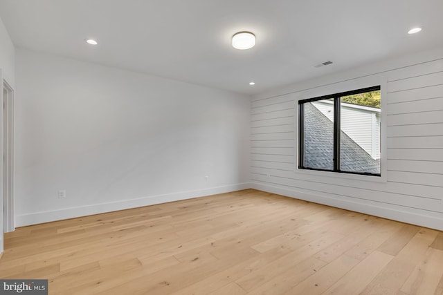 spare room with light hardwood / wood-style flooring and wood walls