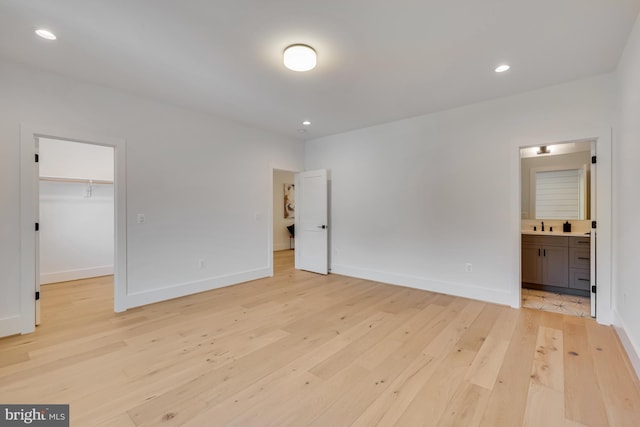 unfurnished bedroom with a spacious closet, light hardwood / wood-style floors, a closet, ensuite bath, and sink