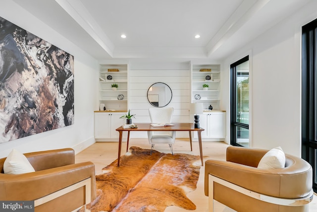 office area with light hardwood / wood-style floors, a tray ceiling, and built in shelves