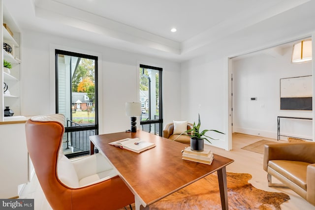 office area with light hardwood / wood-style floors and a tray ceiling