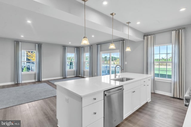 kitchen featuring a wealth of natural light, decorative light fixtures, stainless steel dishwasher, and an island with sink