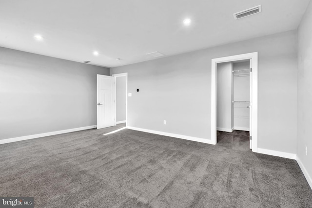 unfurnished bedroom featuring a spacious closet, a closet, and dark colored carpet