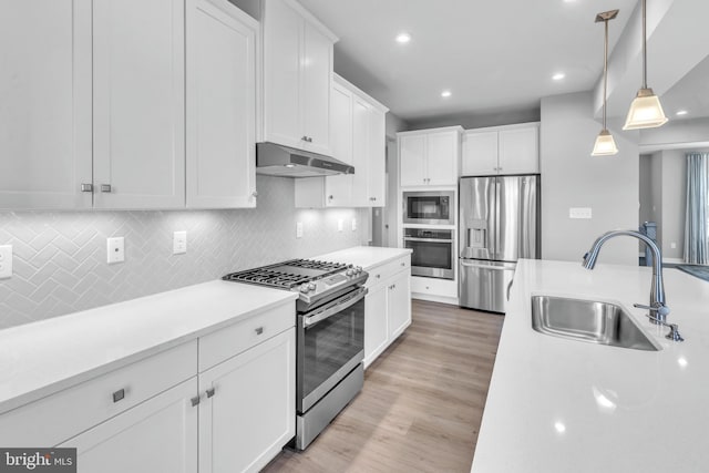 kitchen featuring appliances with stainless steel finishes, white cabinetry, light hardwood / wood-style floors, decorative light fixtures, and sink