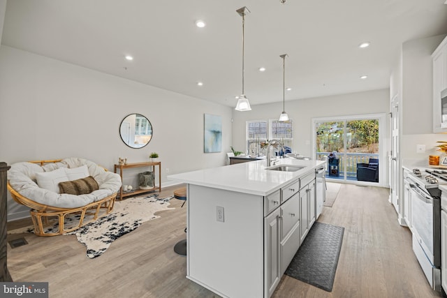 kitchen featuring stainless steel appliances, sink, an island with sink, light hardwood / wood-style flooring, and pendant lighting