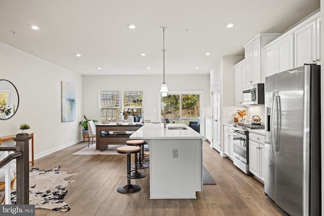 kitchen featuring sink, appliances with stainless steel finishes, an island with sink, white cabinets, and pendant lighting