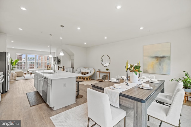 kitchen featuring stainless steel appliances, light hardwood / wood-style floors, a center island with sink, sink, and hanging light fixtures