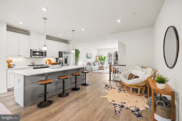 kitchen featuring stainless steel appliances, white cabinetry, decorative light fixtures, an island with sink, and light hardwood / wood-style floors