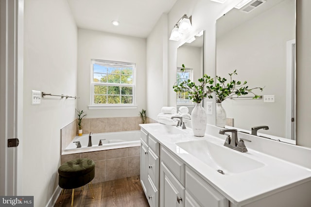 bathroom with hardwood / wood-style floors, vanity, and a relaxing tiled tub