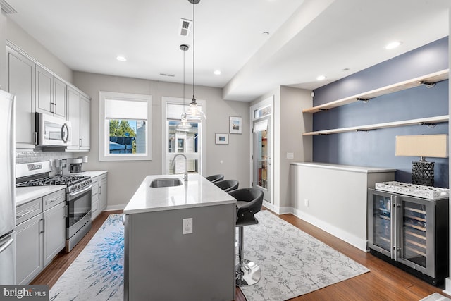 kitchen featuring an island with sink, hanging light fixtures, wine cooler, sink, and appliances with stainless steel finishes