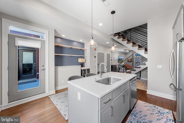 kitchen featuring hardwood / wood-style floors, an island with sink, appliances with stainless steel finishes, gray cabinets, and sink