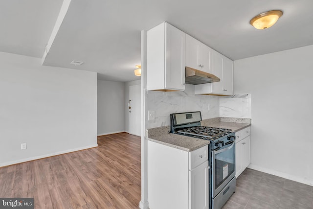 kitchen with decorative backsplash, light stone counters, stainless steel gas range, white cabinets, and light hardwood / wood-style floors