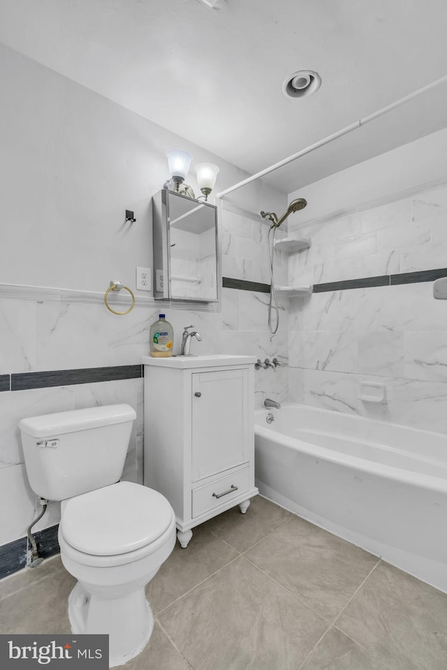 full bathroom with vanity, tile patterned floors, tiled shower / bath, toilet, and tile walls