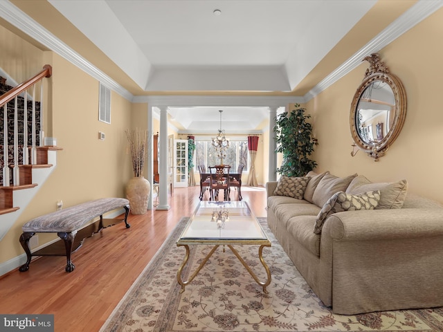 living area featuring decorative columns, stairway, ornamental molding, wood finished floors, and a tray ceiling