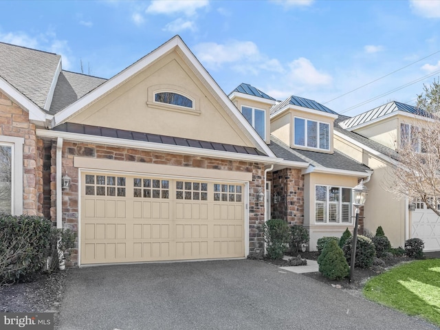 view of front of property featuring metal roof, an attached garage, stone siding, stucco siding, and a standing seam roof