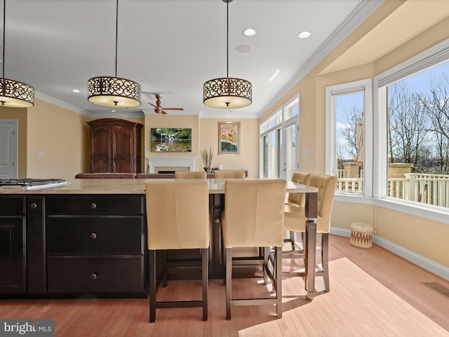 kitchen featuring baseboards, hanging light fixtures, dark cabinetry, light wood-type flooring, and crown molding