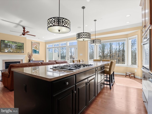 kitchen featuring stainless steel gas cooktop, a fireplace, dark cabinetry, light wood-type flooring, and crown molding