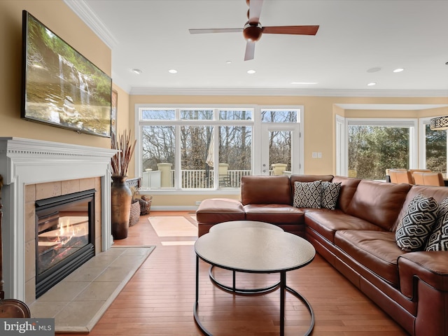 living area with ornamental molding, plenty of natural light, a tile fireplace, and light wood-style flooring