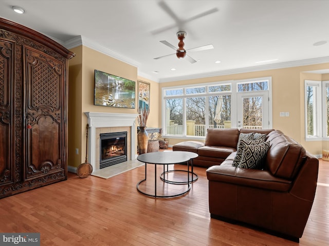 living area with light wood finished floors, a tiled fireplace, and crown molding