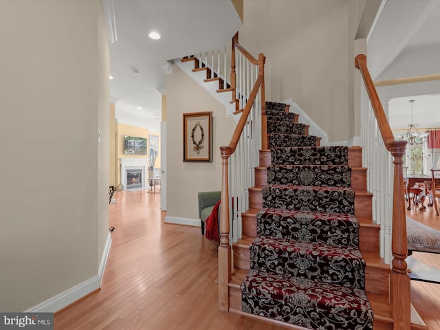 stairway featuring a chandelier, recessed lighting, baseboards, wood-type flooring, and a glass covered fireplace