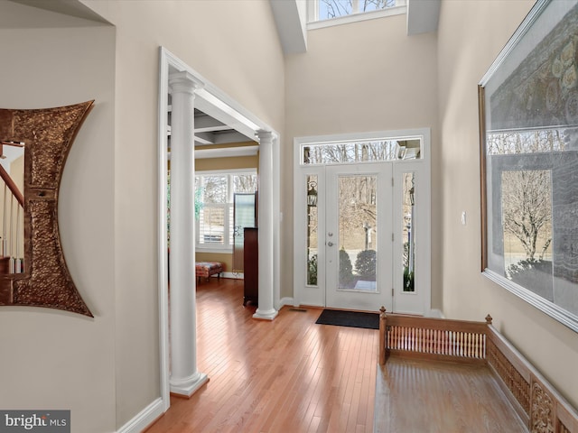 entryway with light wood-style floors, baseboards, a high ceiling, and ornate columns