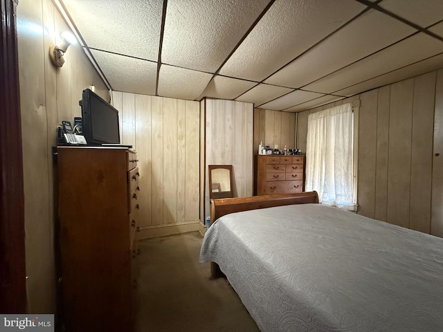 carpeted bedroom featuring wooden walls and a paneled ceiling