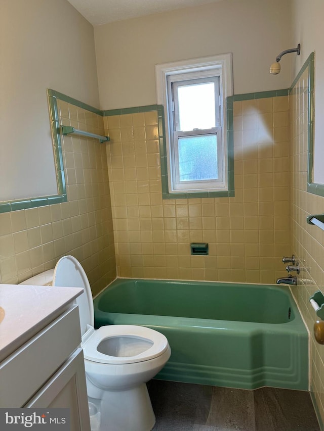 full bathroom featuring tile walls, vanity, tiled shower / bath combo, and toilet