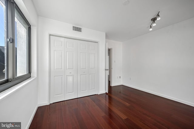 unfurnished bedroom featuring a closet, dark hardwood / wood-style flooring, and rail lighting