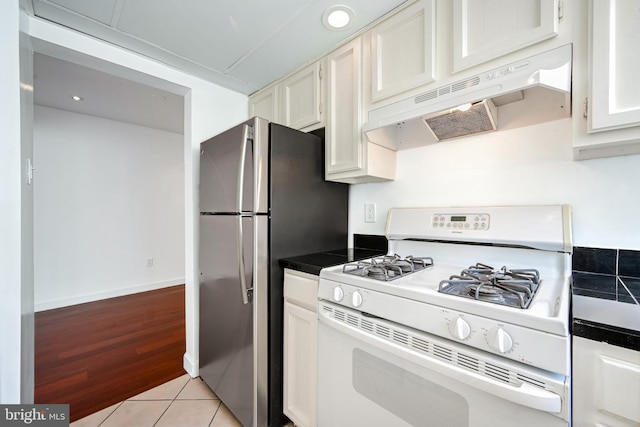 kitchen featuring white cabinets, white range with gas stovetop, stainless steel fridge, extractor fan, and light tile patterned floors