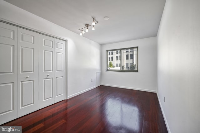 unfurnished bedroom featuring dark hardwood / wood-style floors, rail lighting, and a closet