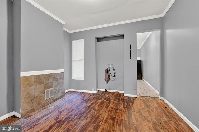 empty room featuring tile walls, ornamental molding, and hardwood / wood-style floors