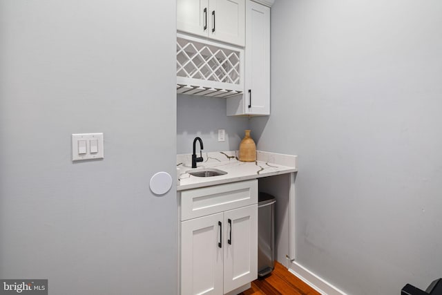 bar with hardwood / wood-style flooring, light stone countertops, sink, and white cabinets