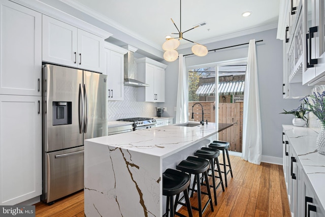 kitchen with appliances with stainless steel finishes, an island with sink, hanging light fixtures, white cabinetry, and hardwood / wood-style flooring