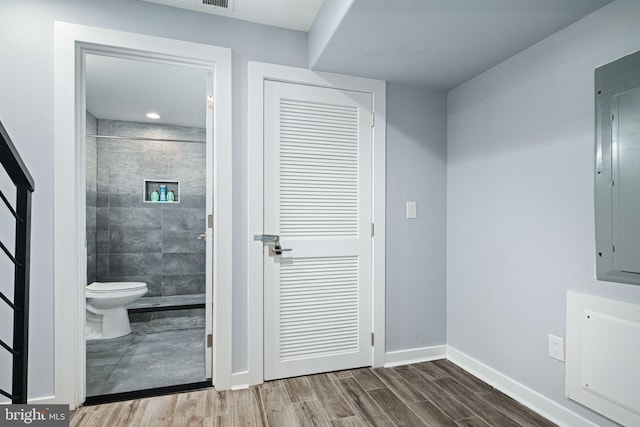 bathroom with toilet, electric panel, tiled shower, and hardwood / wood-style floors